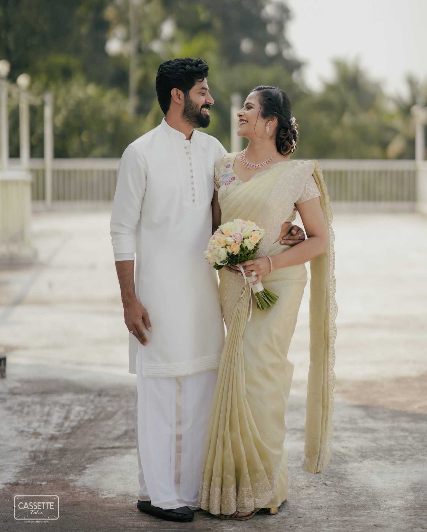A couple smiling at each other in traditional ivory attire