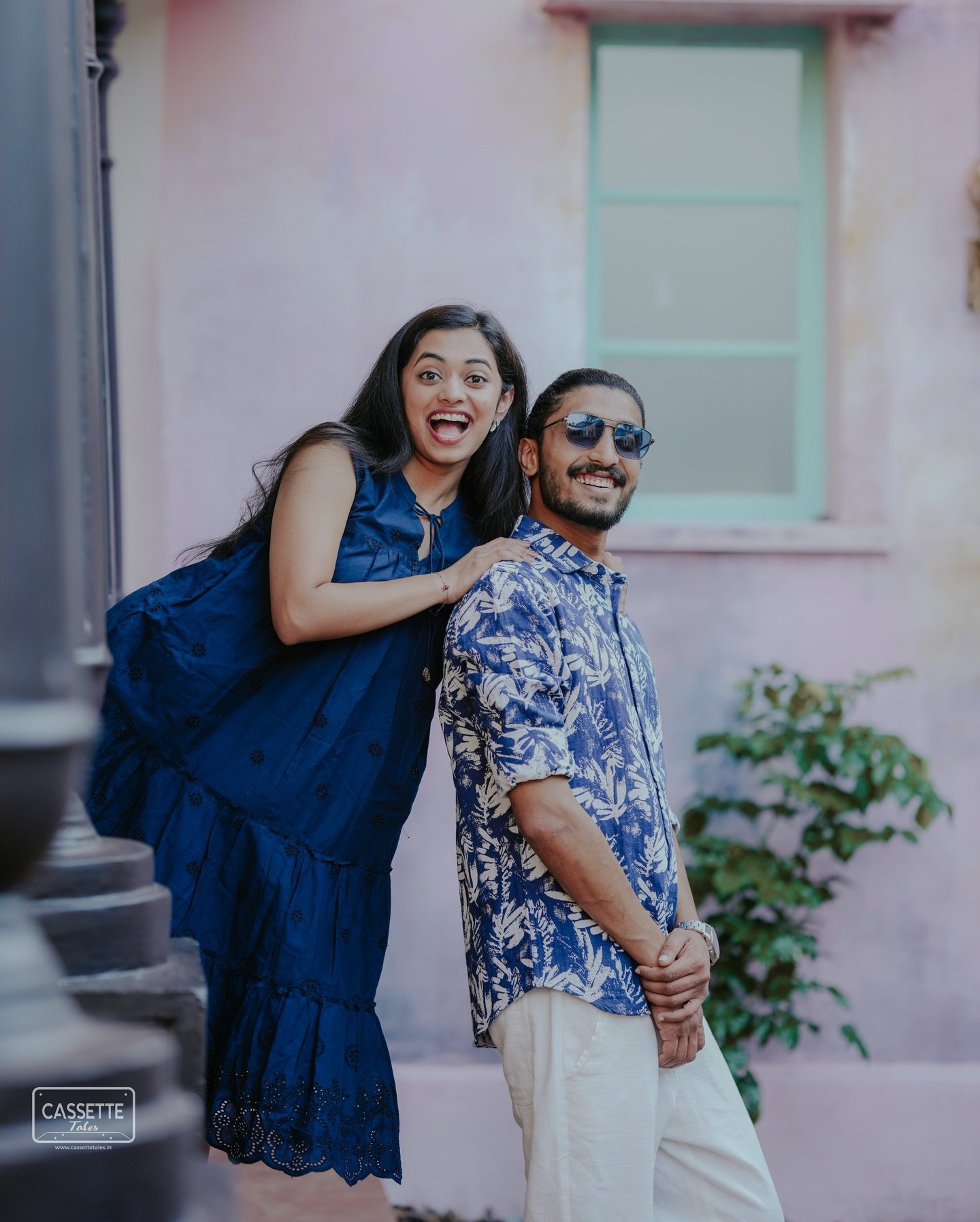 A playful couple posing together in front of a pastel building