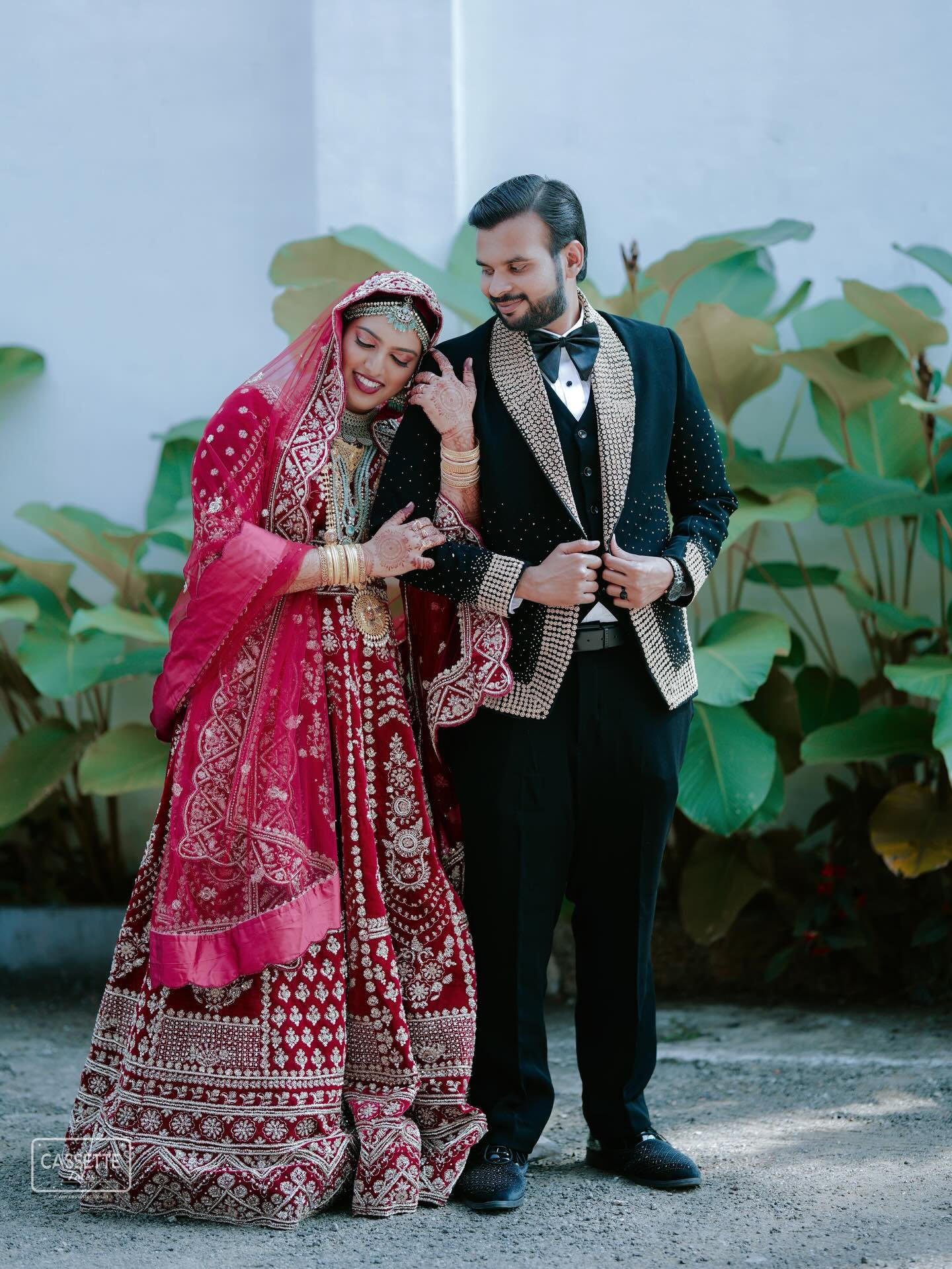 A newlywed couple standing together in front of lush greenery